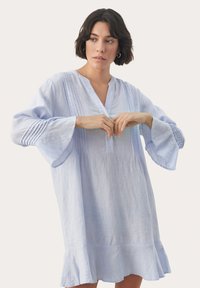 Rochie din in bleu deschis, cu decolteu în V, detalii plisate și mâneci evazate. Prezintă un tiv ondulat și accente subtile texturate.