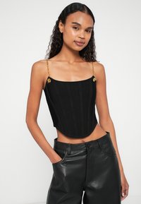 Μαύρο κοντό τοπ με κάθετη ριγωτή υφή, που διαθέτει χρυσές αλυσίδες στους ώμους και διακοσμητικές λεπτομέρειες. Συνδυάζεται με μαύρο δερμάτινο παντελόνι.