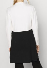 Long-sleeve cardigan with a color-block design; top section is white, bottom is black. Soft texture, mid-length cut, no visible hardware.