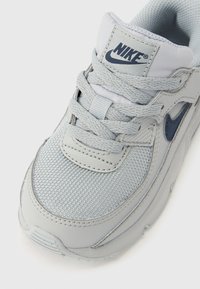 Szürke sportcipő texturált hálós felsőrésszel, bőr díszítésekkel és kék Nike logóval. Párnázott szegéllyel és cipőfűzőkkel biztosított rögzítés.