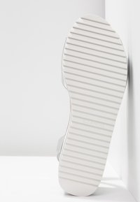 Semelle blanche d'une sandale avec des stries horizontales, présentée verticalement sur un fond blanc avec l'inscription "CALL IT SPRING" embossée près du talon.