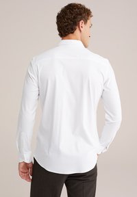 Witte blouse met lange mouwen en een overlappende kraag, met een gladde textuur, met knoopmanchetten en een gebogen zoom. Gemaakt met donkere broeken.