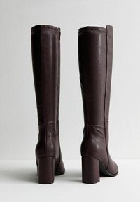 Stivali alti fino al ginocchio in pelle marrone con tacco a blocco, caratterizzati da una texture liscia e da una chiusura con zip esterna. Design semplice ed elegante.