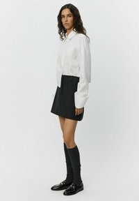 White button-up shirt with a cropped cut, paired with a dark gray skirt. Model wears knee-high gray socks and black loafers.