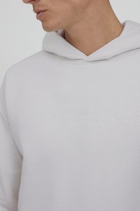 Weißer Baumwoll-Hoodie mit Kängurutasche und gesticktem Markenlogo auf der Brust. Verfügt über eine traditionelle Kapuze mit Zugband. Weicher Stoff.