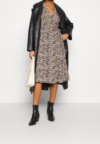 Kwiatowa midi sukienka w kolorze czarnym z wielokolorowymi kwiatami, dekolt w serek, ściśnięta talia. Noszona z czarnym skórzanym płaszczem i czarnymi botkami za kostkę.