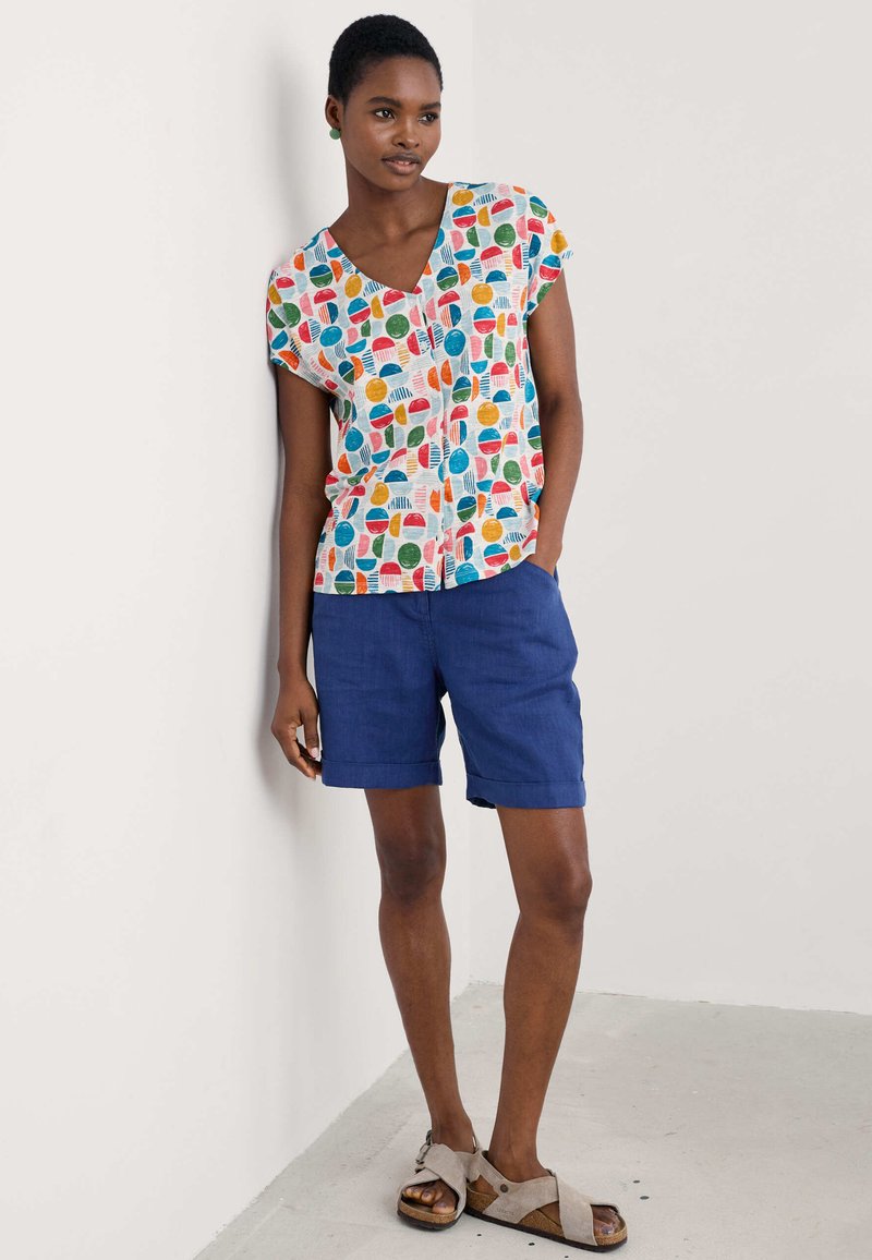 Short-sleeve top in white with colorful circular patterns, paired with blue knee-length shorts and beige sandals with adjustable straps.