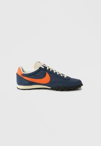 Blauer und orangefarbener Nike-Sneaker mit strukturierter Oberseite, weißen Schnürsenkeln und einer Gummisohle mit schwarzen Noppen für besseren Halt.