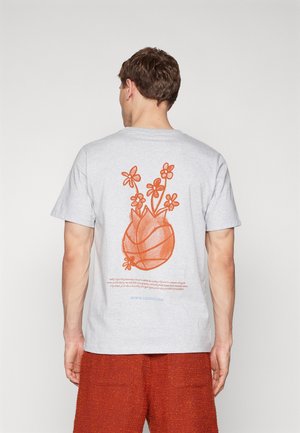 Homme vu de dos portant un t-shirt gris clair avec un graphisme orange représentant un ballon de basket et une fleur au dos, associé à un short orange texturé.
