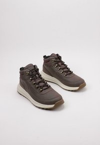 Botas de senderismo marrones con un material superior suave, diseño de cordones y suela de goma. Presenta herrajes de metal y un collar acolchado para mayor soporte.