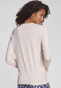 Light pink long-sleeve top with a rounded neckline, smooth texture, and a relaxed fit, paired with patterned blue bottoms.