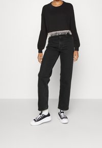 Felpa nera corta con orlo a frange di perline, abbinata a jeans neri a vita alta e sneakers di tela nere con suole bianche.