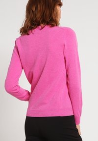 Pull en tricot fuchsia à manches longues, col rond et ourlet côtelé. Texture douce, coupe ajustée et finition lisse.