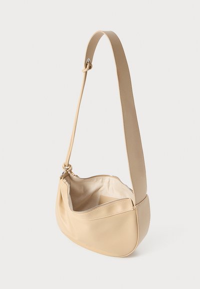 Sac à épaule en cuir beige avec une texture lisse, une forme courbée, une sangle unique réglable et une fermeture éclair. L'intérieur est non doublé.