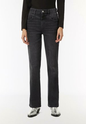 Osoba nosząca czarne jeansy o prostych nogawkach z przednimi kieszeniami, w połączeniu ze srebrnymi botkami do kostki i czarnym długim rękawem.