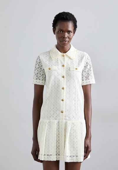 Lace dress in pale yellow with a collar, short sleeves, and gold buttons. Features a pleated skirt and intricate lace pattern.