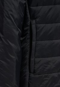 Svart pufferjacka med en slät, glänsande yta, horisontell quiltad design och dolda sidofickor för förvaring.