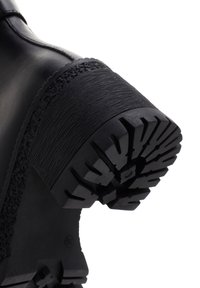 Bota de cuero negro con una suela de goma negra texturizada. El tacón presenta un diseño estriado y un patrón de relieve robusto para mayor tracción.