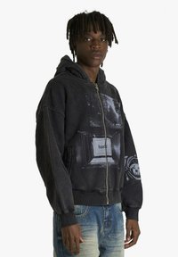 Felpa con cappuccio e zip nera con stampa grafica sul davanti, tessuto testurizzato, tasche frontali e polsini a costine.