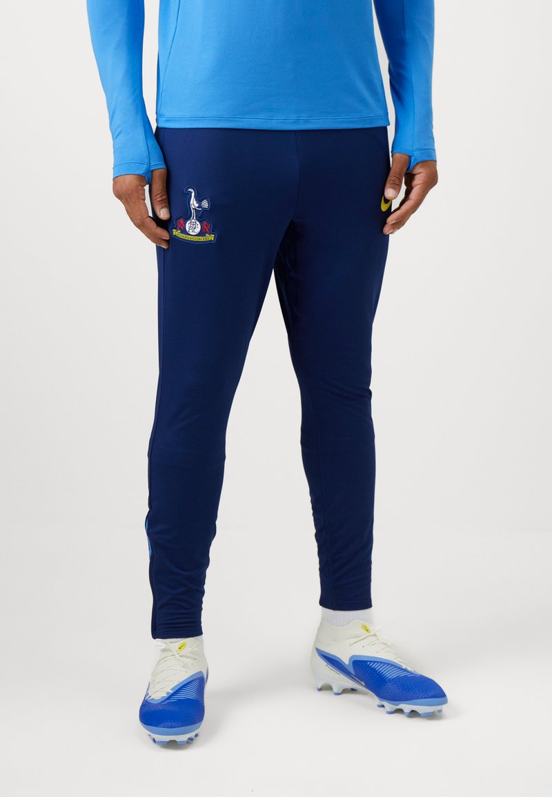 Marinefarbene Sporthosen mit gesticktem Logo und roten sowie gelben Akzenten. Hergestellt aus einem dehnbaren Material, entworfen für Komfort und Beweglichkeit.