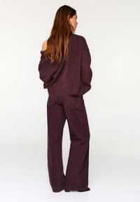 Nagy méretű bordó pulóver vállvillantós dizájnnal, bordázott szegéllyel; széles szárú bordó farmerral párosítva, laza szabással.