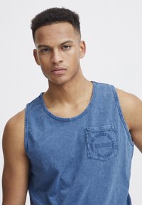 Denim topp i mellomblå farge, med rund halslinning og brystlomme med broderte detaljer. Myk tekstur, avslappet design.