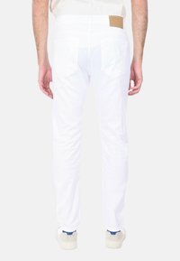 Pantaloni bianchi in cotone con una vestibilità slim, dotati di tasche posteriori e un'etichetta in pelle color crema sulla cintura. Texture liscia e design pulito.