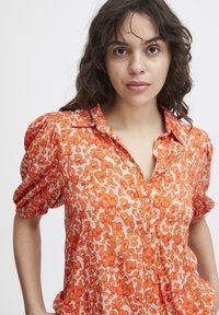 Orange floral-patterned blouse with puffed short sleeves and a button-down front. Lightweight fabric with a soft texture.