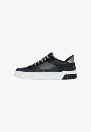 Zapatilla baja en blanco y negro con cordones estampados, talón con purpurina, suela blanca gruesa y acento metálico plateado en la parte posterior del cuello.