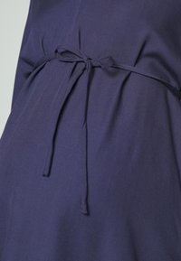 Marinblå plagg med mjuk textur och knytning i midjan. Det släta tyget faller lätt och framhäver form och passform.