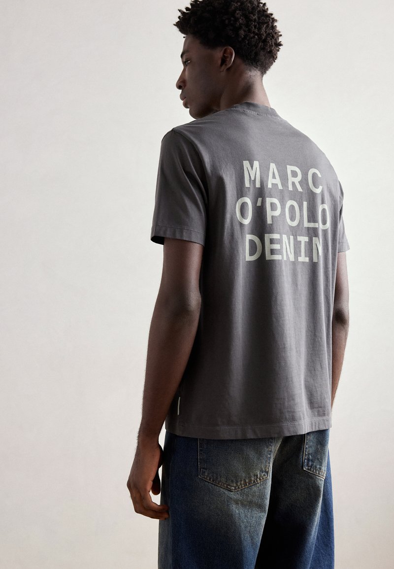 Grijze katoenen T-shirt met "MARC O'POLO DENIM" groot gedrukt op de achterkant in witte letters. Ronde hals, korte mouwen, casual fit.