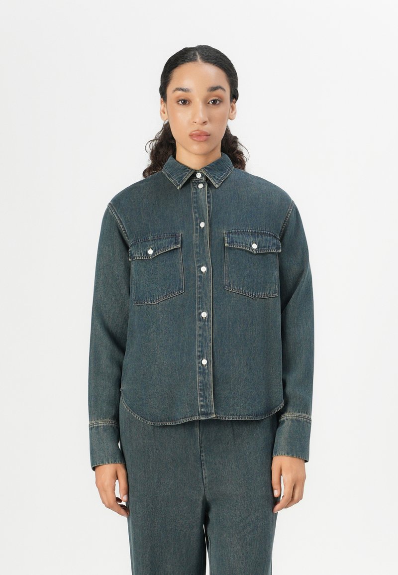 Dunkelblaue Jeanshemd mit einer durchgehenden Knopfleiste, zwei Brusttaschen und einem Kragen. Besitzt sichtbare Nähte und einen lockeren Schnitt.