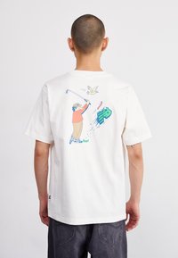 New Balance ATHLETICS RELAXED GOLF CARTOON - Apdrukāts T-krekls - sea salt