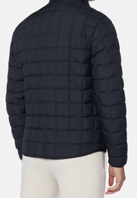 Marinblått pufferjacka med ett kviltat mönster. Har hög krage och elastiska cuffs. Materialet verkar slätt och lätt, med en figurnära passform.