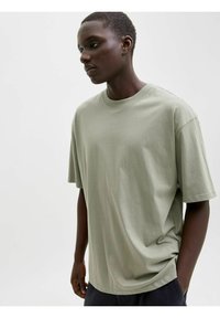 Jasnozielona, oversize koszulka z wysokiej jakości bawełny, z okrągłym dekoltem i krótkimi rękawami, o gładkiej, matowej teksturze.
