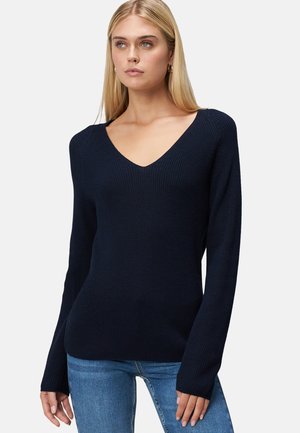 Pull en tricot bleu marine avec un col en V, manches longues, texture côtelée et silhouette ajustée, associé à un jean bleu clair.