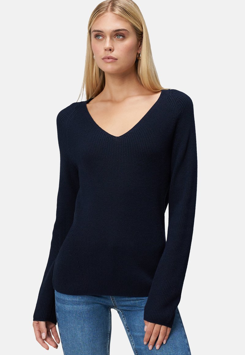 Pull en tricot bleu marine avec un col en V, manches longues, texture côtelée et silhouette ajustée, associé à un jean bleu clair.