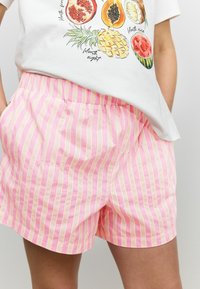 Shorts rayés rose et crème en coton, avec une taille élastique et des poches latérales, présentant une coupe décontractée et une texture légère.