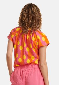 Buntes Hemd mit einem leuchtend pinken Hintergrund und gelben, zitronenförmigen Mustern, kurzen Ärmeln und einem gerafften Rückendesign.