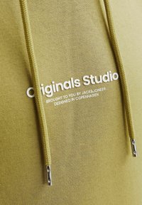 Olivegrüner Kapuzenpullover mit strukturiertem Stoff, Kordelzug mit metallischen Enden und einem Frontdruck, auf dem "Originals Studio" steht.