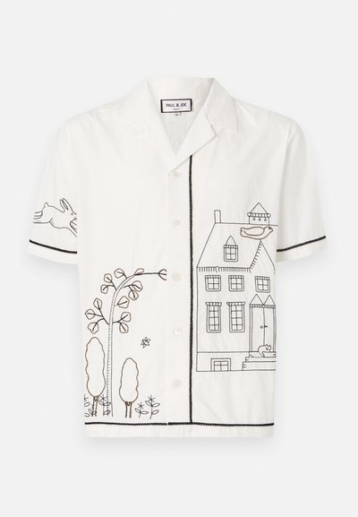 Chemise blanche à manches courtes ornée d'une broderie en contour noir représentant une maison, des arbres et un lapin. Fermeture à boutons sur le devant et bords contrastants.