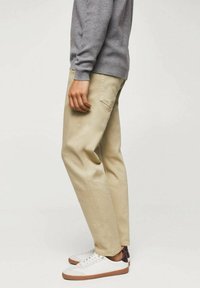 Chinos de algodón beige con un corte relajado, que presentan bolsillos laterales y una textura sutil, combinados con zapatillas blancas y marrones.