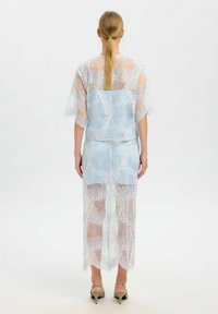 Ensemble deux pièces en dentelle bleu clair comprenant un haut à manches courtes évasées et une longue jupe avec un ourlet festonné et une texture transparente.