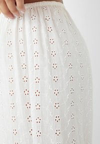 Vitt broderat kjol med utskurna blommönster, en rynkad elastisk midja och ett lätt, texturerat tyg.