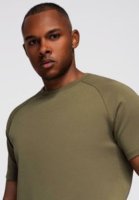 Oliven grøn kortærmet t-shirt lavet af glat stof, med rund hals og raglanærmer, i en tætsiddende design og minimal syning.