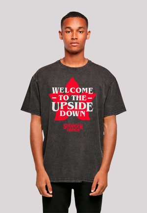 Black graphic t-shirt with short sleeves featuring a red star and white text that reads "WELCOME TO THE UPSIDE DOWN STRANGER THINGS."
