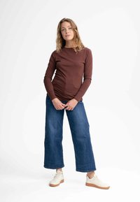 Brauner langärmeliger Oberteil, kombiniert mit weitgeschnittenen blauen Jeans und weißen Sneakers mit brauner Sohle. Einfaches, körperbetontes Design mit Rundhalsausschnitt.