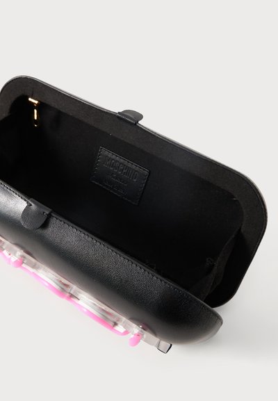 Μαύρο δερμάτινο clutch Moschino ανοιχτό για να δείξει κενό εσωτερικό με ετικέτα της μάρκας, σε απλό ανοιχτό φόντο.