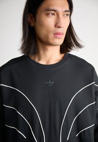 Black sweatshirt with white accent lines and embroidered logo. Soft fabric, crew neck design, and minimalistic aesthetic.