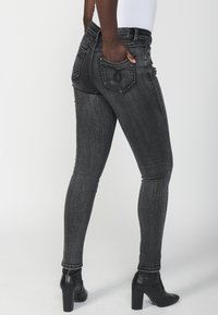 Črne skinny hlače z visokim pasom in zbledelim izgledom, s petimi žepi in kontrastnim šivom, v kombinaciji z črnimi škornji na visoki peti.